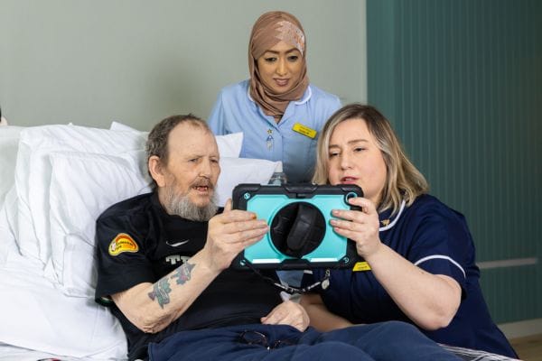 Jaheda, a healthcare assistant, and another nurse showing a patient an iPad and how to listen to audiobooks on it.