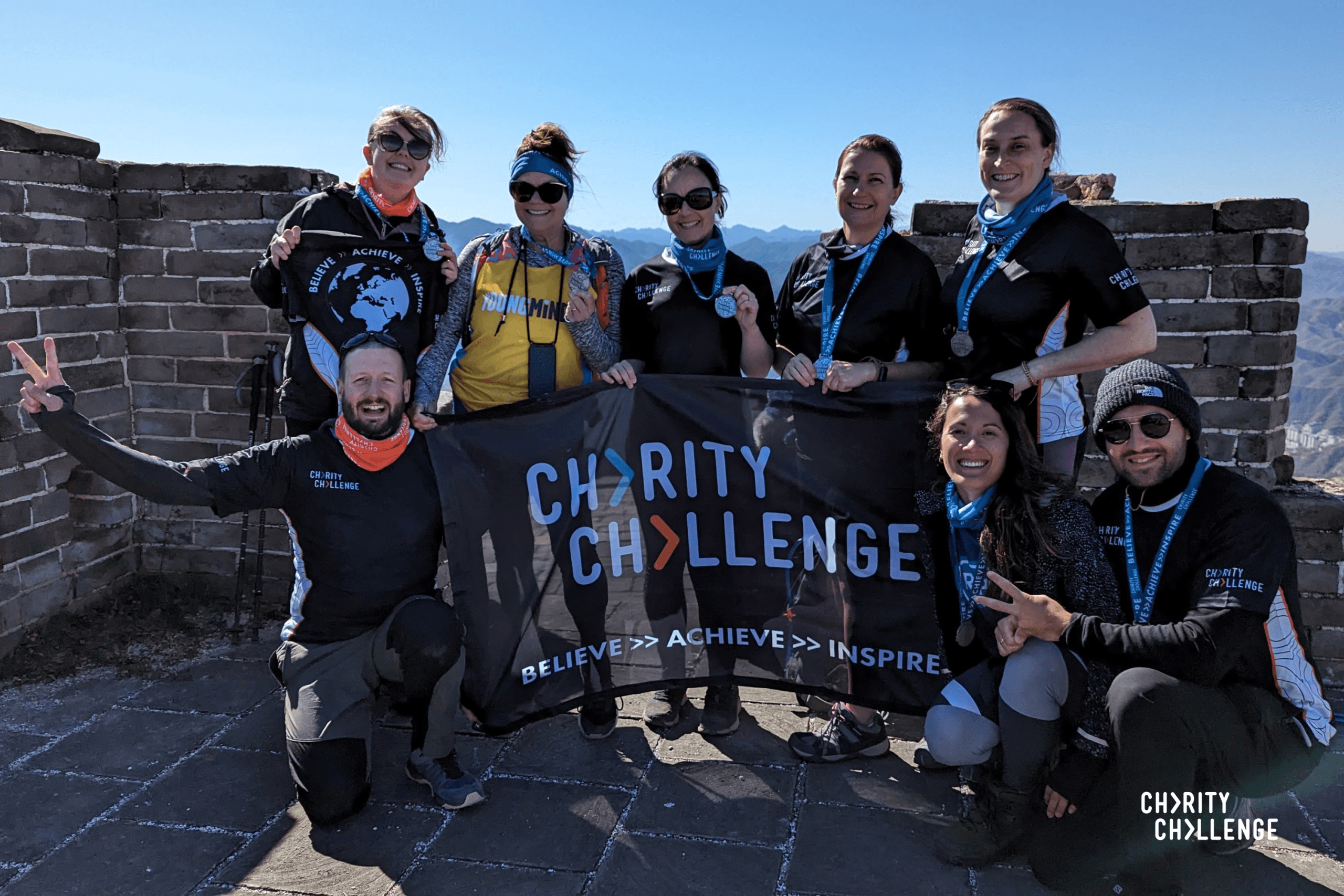 People posing on the Great Wall of China, holding a sign that says 'Charity Challenge'