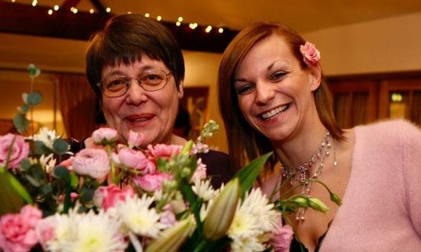 Alex with her mum Paula smiling and looking happy together. Paula is holding a bunch of flowers.