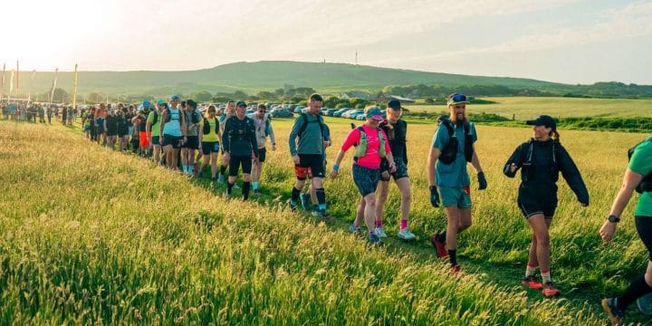 walkers setting off from the start line of the Isle of Wight walking challenge. They're walking across a grassy field with hills in the background