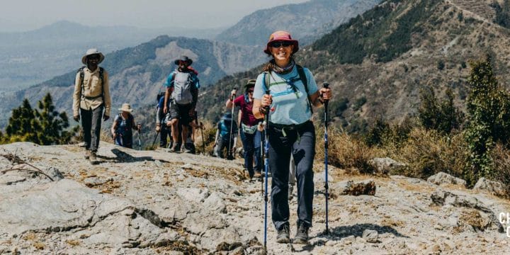 Woman standing on a rocky outcrop overlooking the Himalayan mountains. A group of walkers are behind