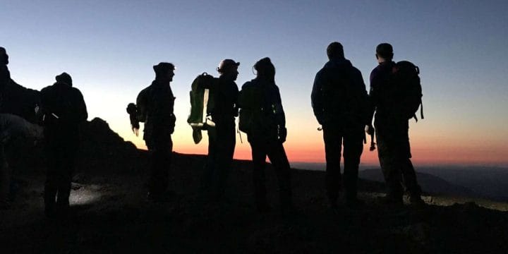 Group of walkers atop a hill in silhouette against a sunset