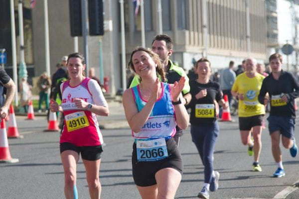 A runner in a martlets vest in a mass-participation running event in Brighton. She is smiling and clapping