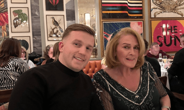 Man in his thirties wearing a black jumper sitting with his mum, a lady in her sixties with light brown hair, wearing a black and silver top. They are sitting in a cafe.