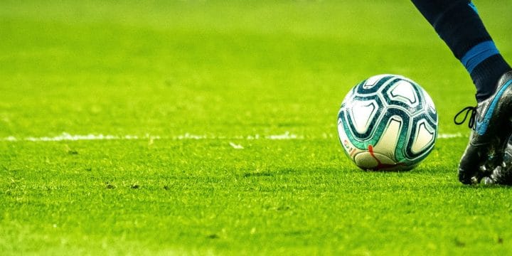 person in football boots and socks picking a football