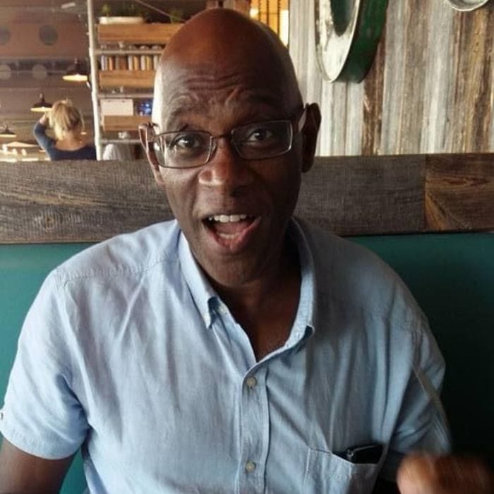 Derrick with a plate of food in a restaurant, he is smiling in an animated way at the camera