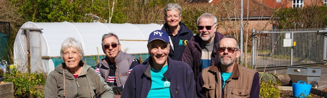 A group of volunteers stands in gardens and smiles at the camera