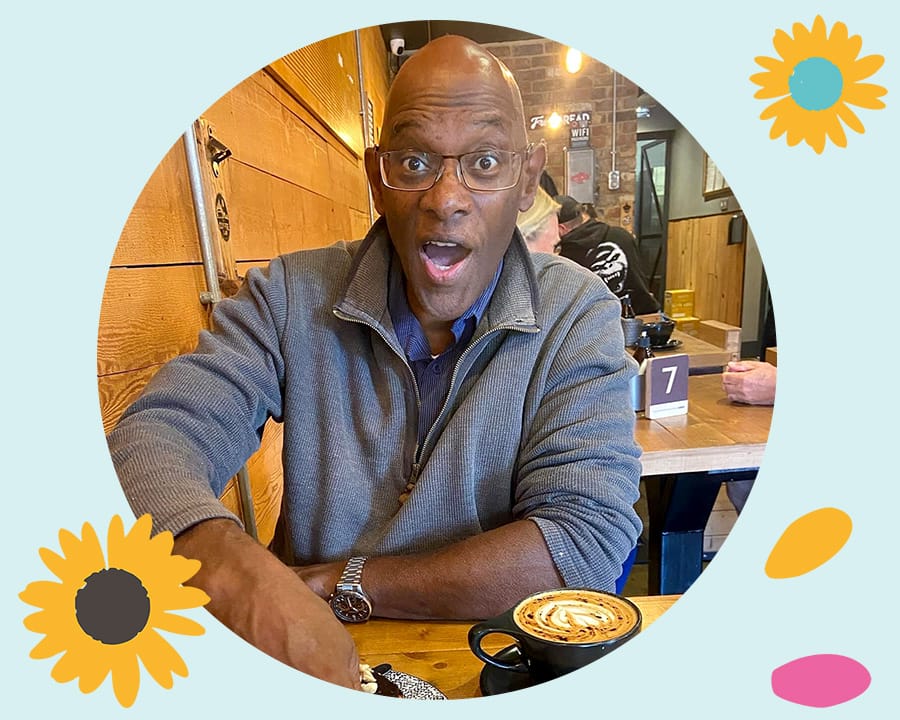Derrick in a cafe pulling a face at the camera. He is surrounded with graphics of sunflowers and petals