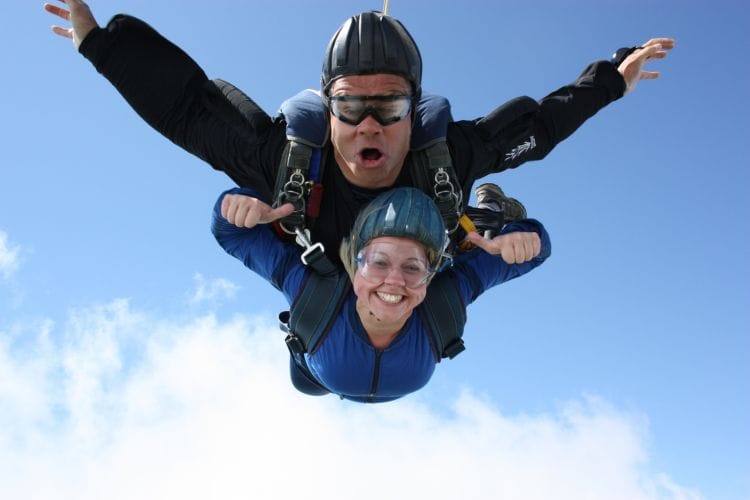 two people skydiving in tandem, with blue skies behind them