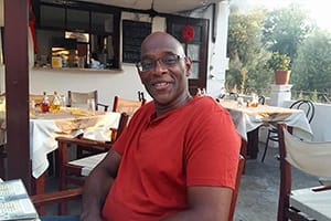 Derrick sitting at a table outside a restaurant, smiling at the camera