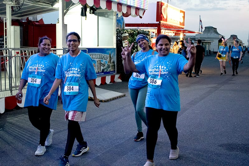 A group of walkers taking part in night to remember, wakling along the prom, smiling and giving peace signs to the camera