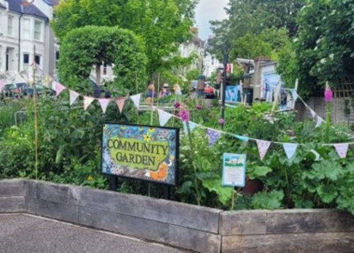 A community garden with lush greenery and flowers. Colourful sign reads "Community garden" and it is surrounded by bunting