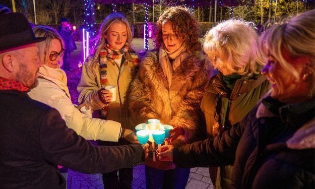Attendees at a Light up a Life service, sitting in an outdoor marquee and holding candles. A white heart holds the text "Light Up a Life"